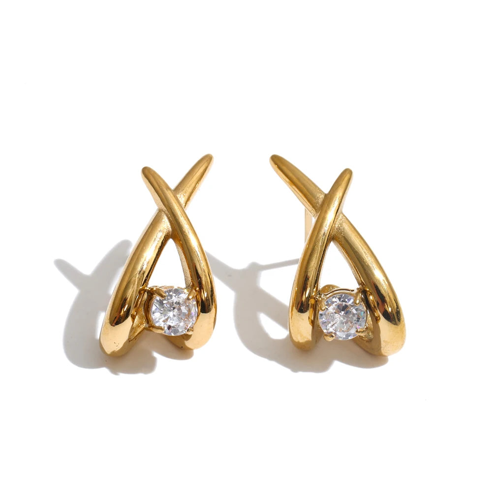 A pair of gold huggie hoop earrings with a single round clear gemstone in each earring, set against a plain white background with soft shadows.