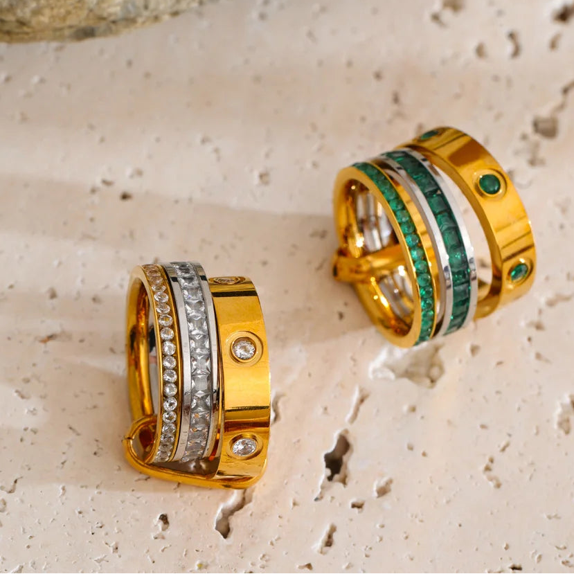 Two gold rings with gemstone inlay on a textured stone surface