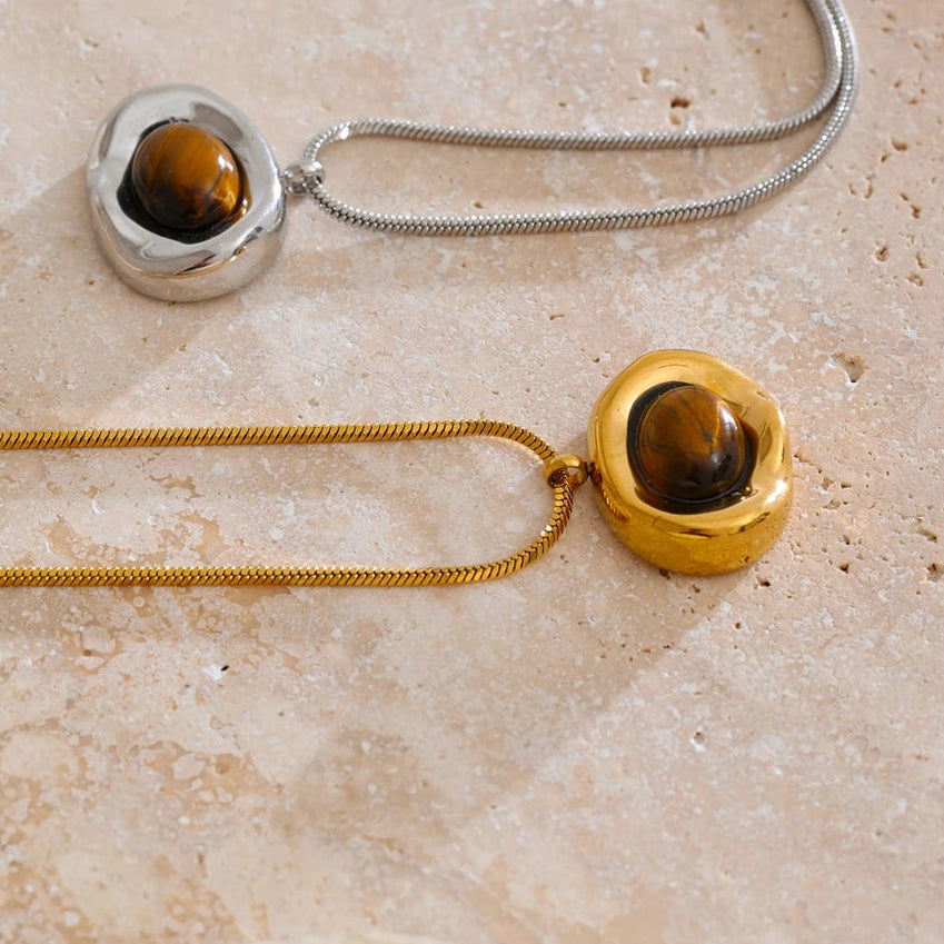 Two necklaces with round pendants on a beige stone surface