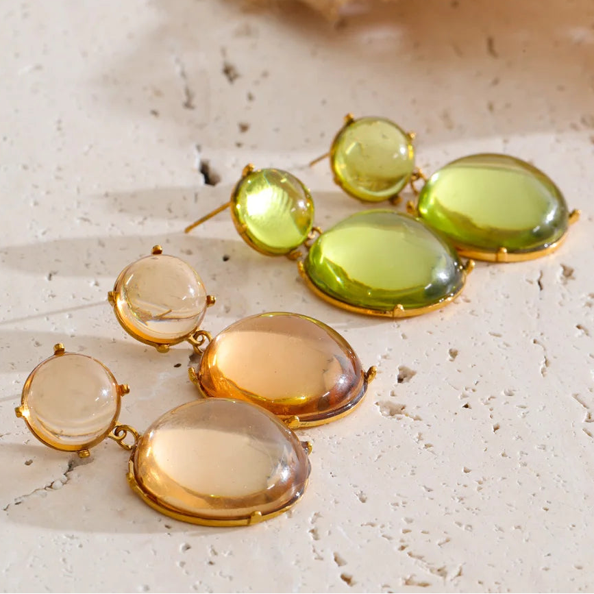 Pair of earrings with green and gold stones on a textured surface
