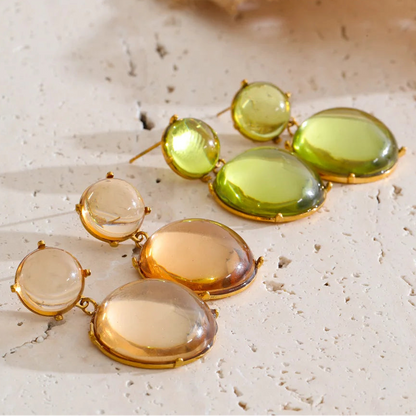 Pair of earrings with green and gold stones on a textured surface