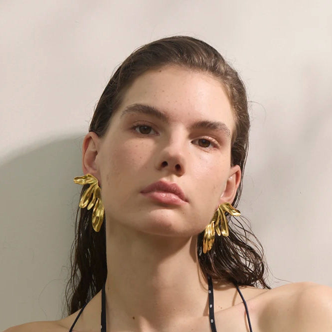 Woman wearing a black polka dot dress with gold earrings against a plain background