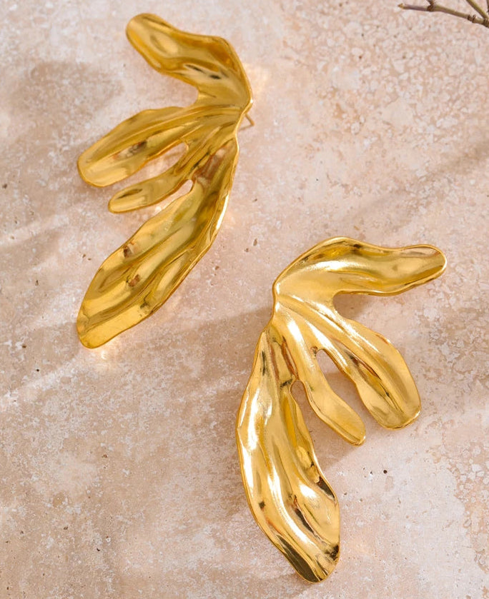 Gold leaf-shaped earrings on a beige stone surface