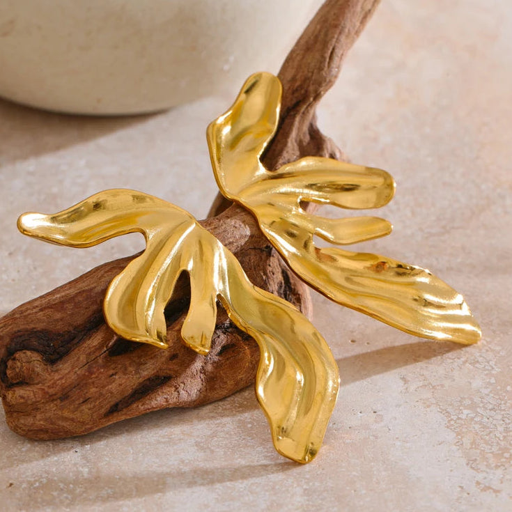Gold leaf-shaped earring on a natural wood and stone background