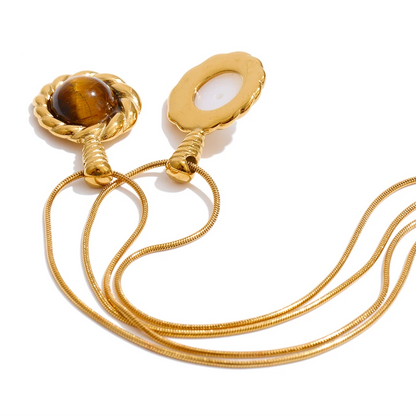 A gold-toned snake chain necklace with two oval pendant settings, one featuring a brown tiger's eye stone and the other with a white inlay