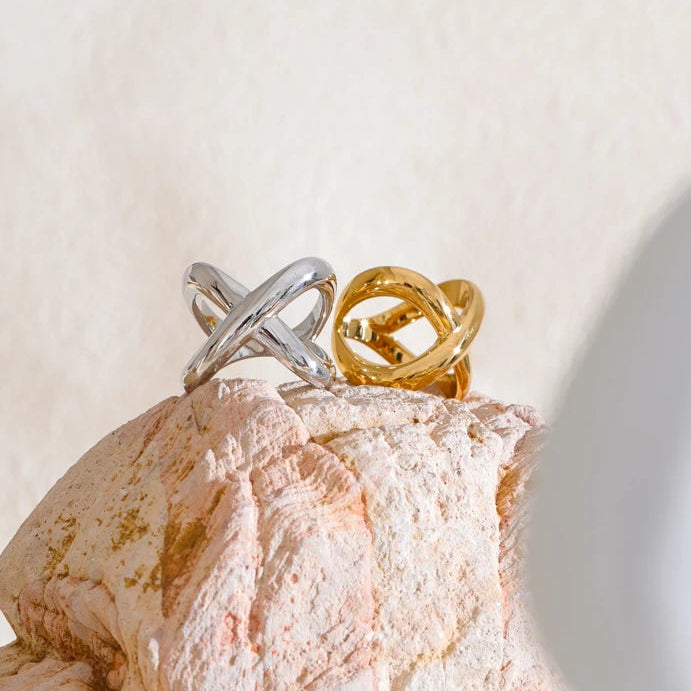 Two rings, one silver and one gold, on a textured stone surface with a soft light background.