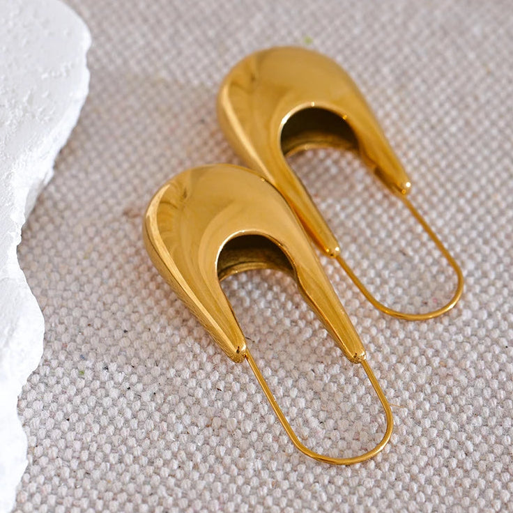 Gold earrings on a textured beige surface